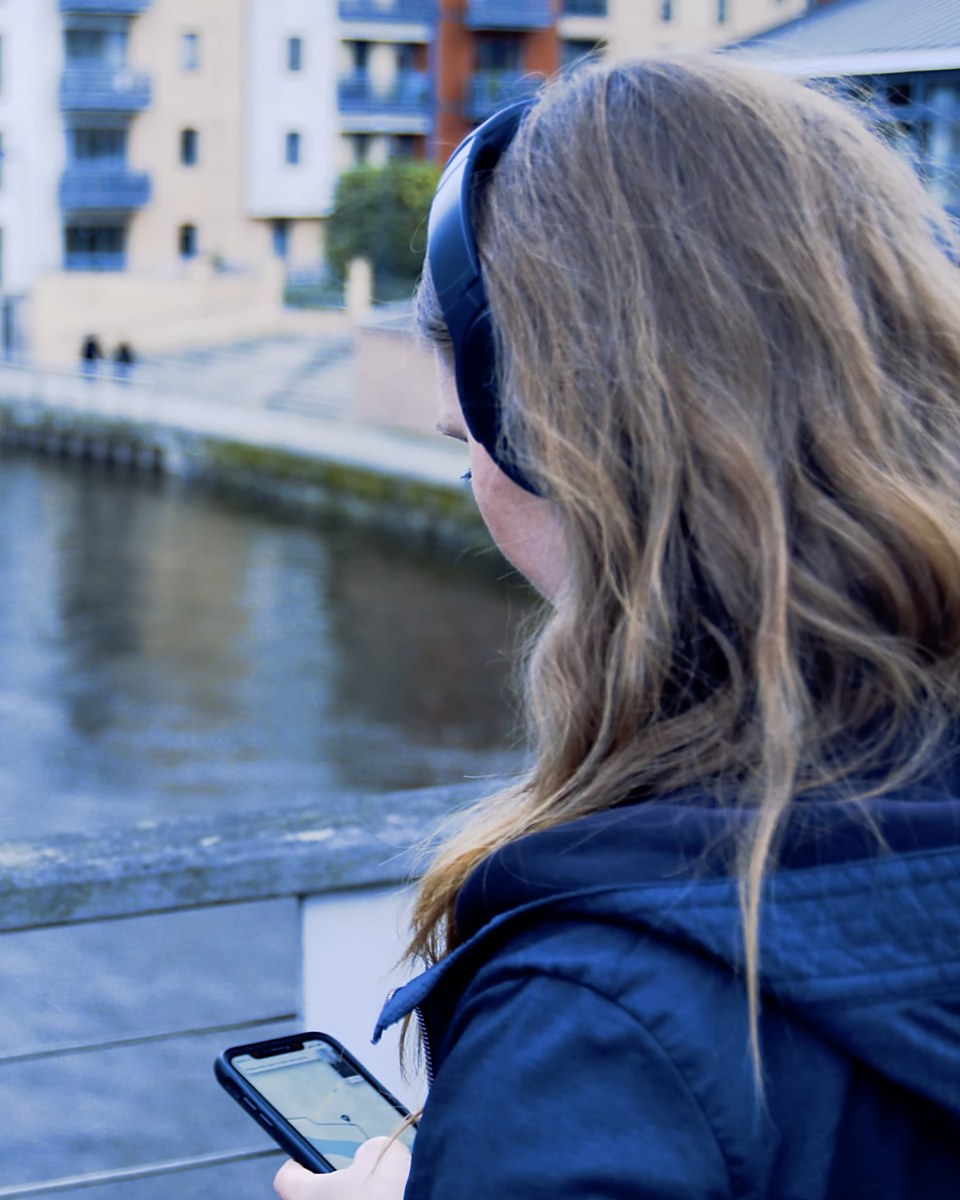 Sonder: an audience member on a bridge over the river in Leeds, headphones on, following a map on her phone